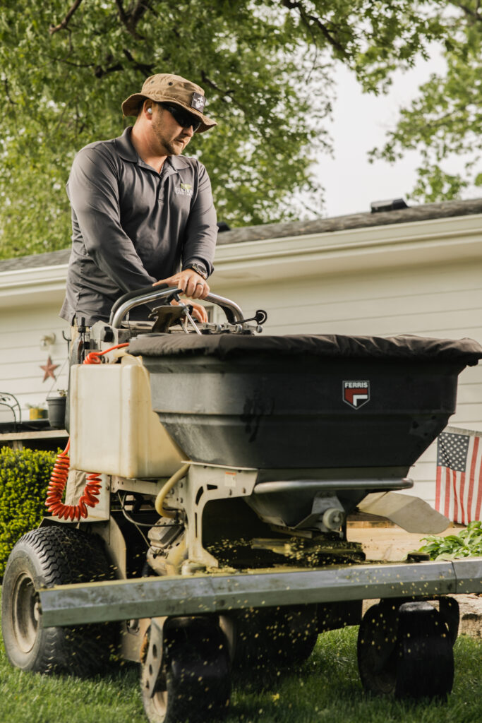 Landscaper operating a large spreader on lawn near white house and American flag