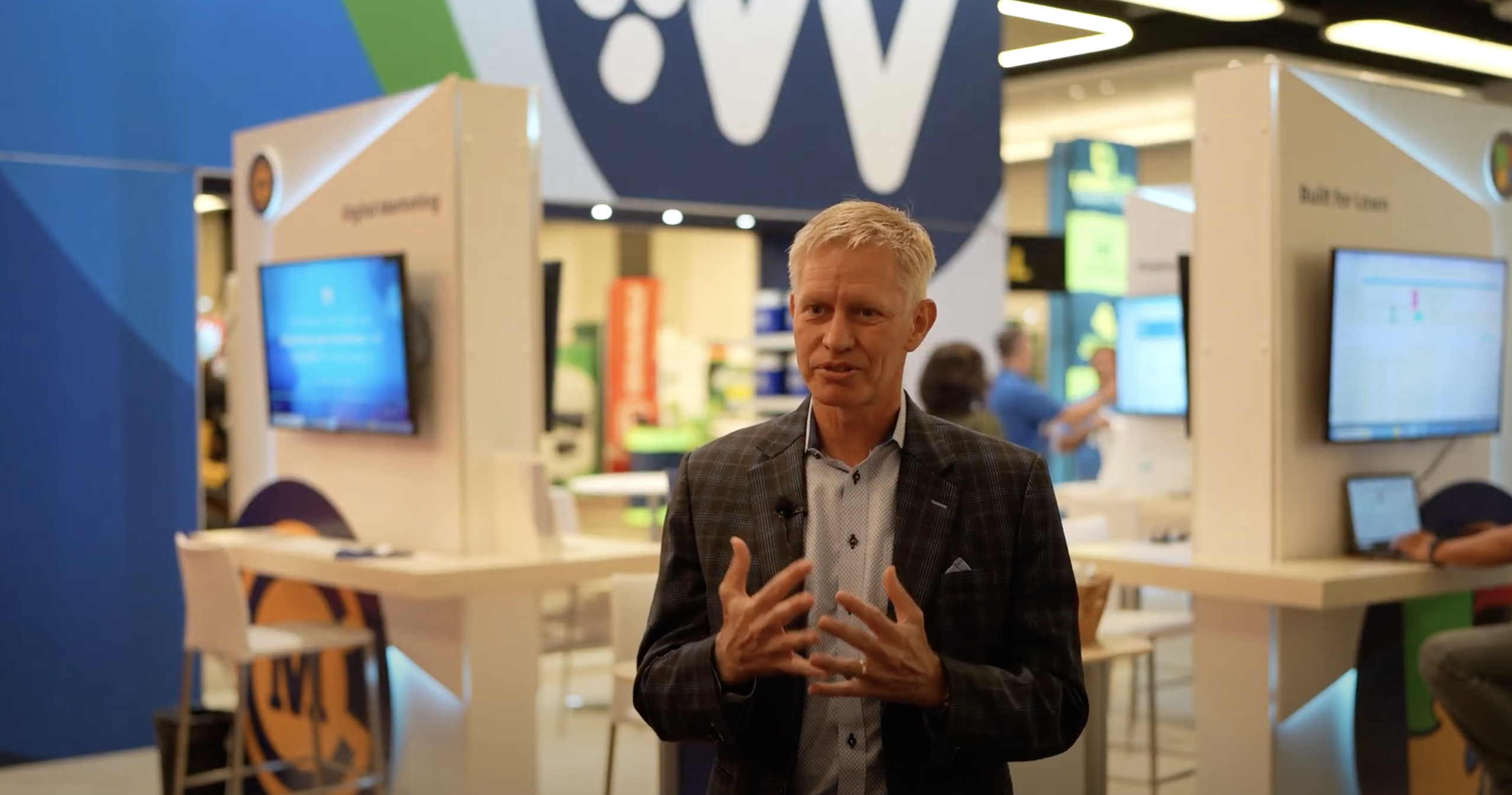 Businessman presenting at technology conference with digital displays behind