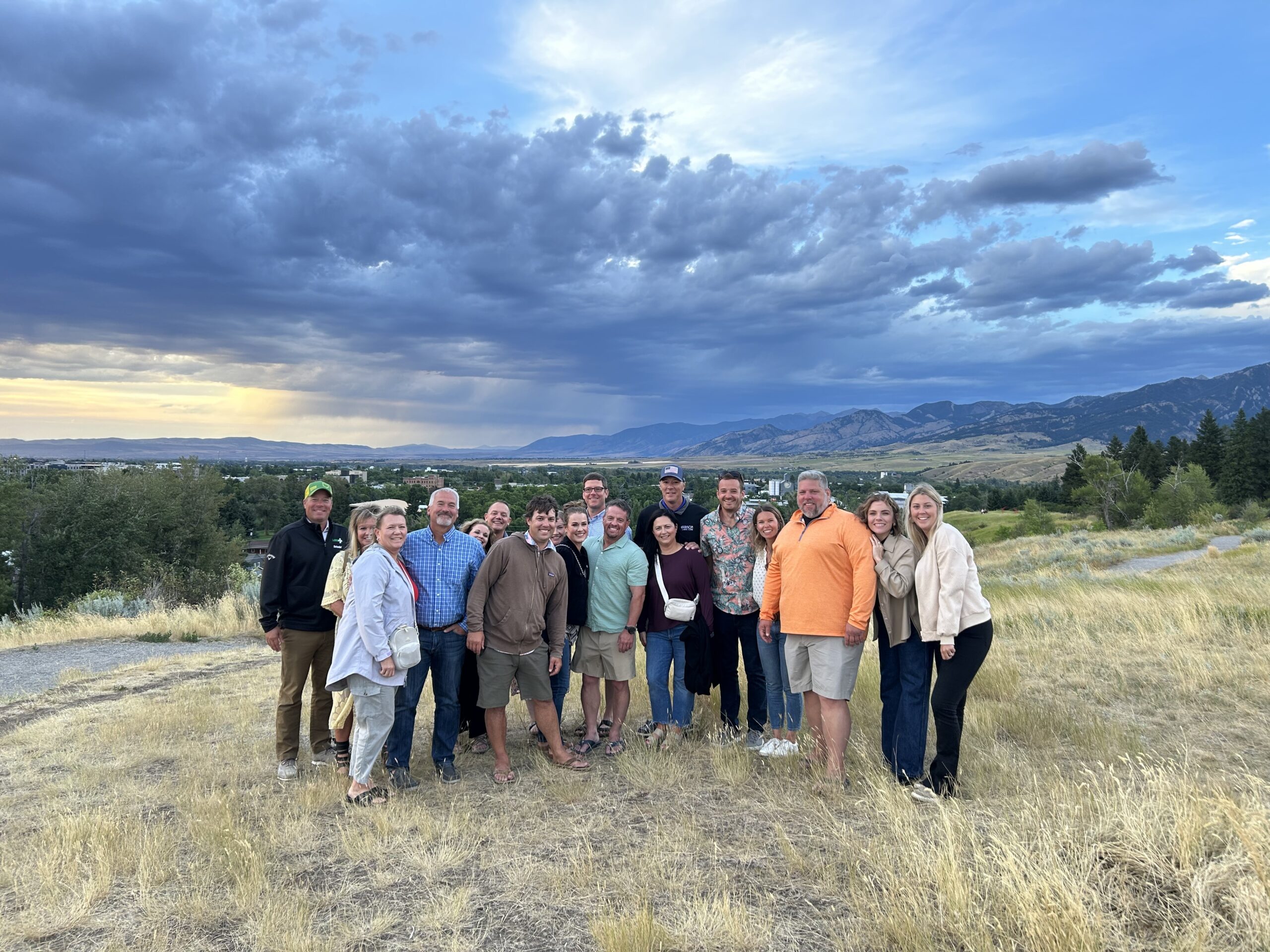 Group photo of people on grassy hill with dramatic mountain and cloud backdrop