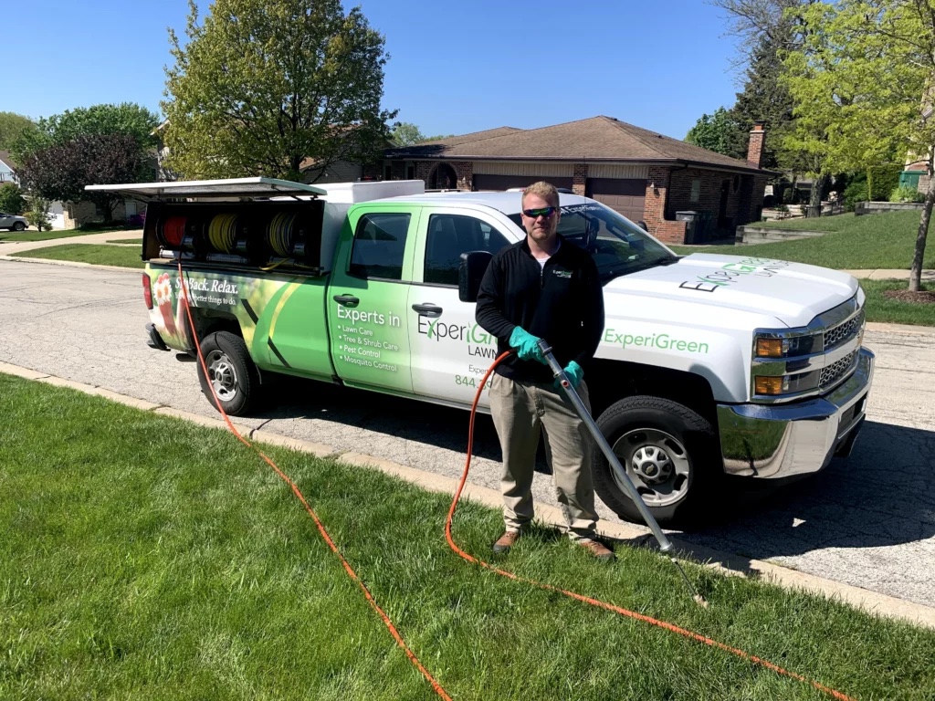ExperiGreen lawn care technician standing next to service truck with hose