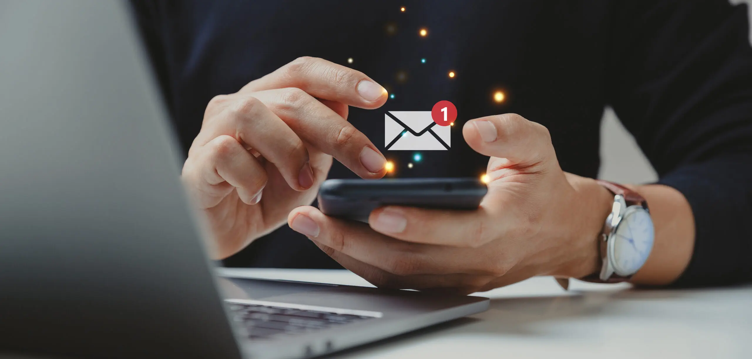 Person checking email on smartphone with notification icon near laptop