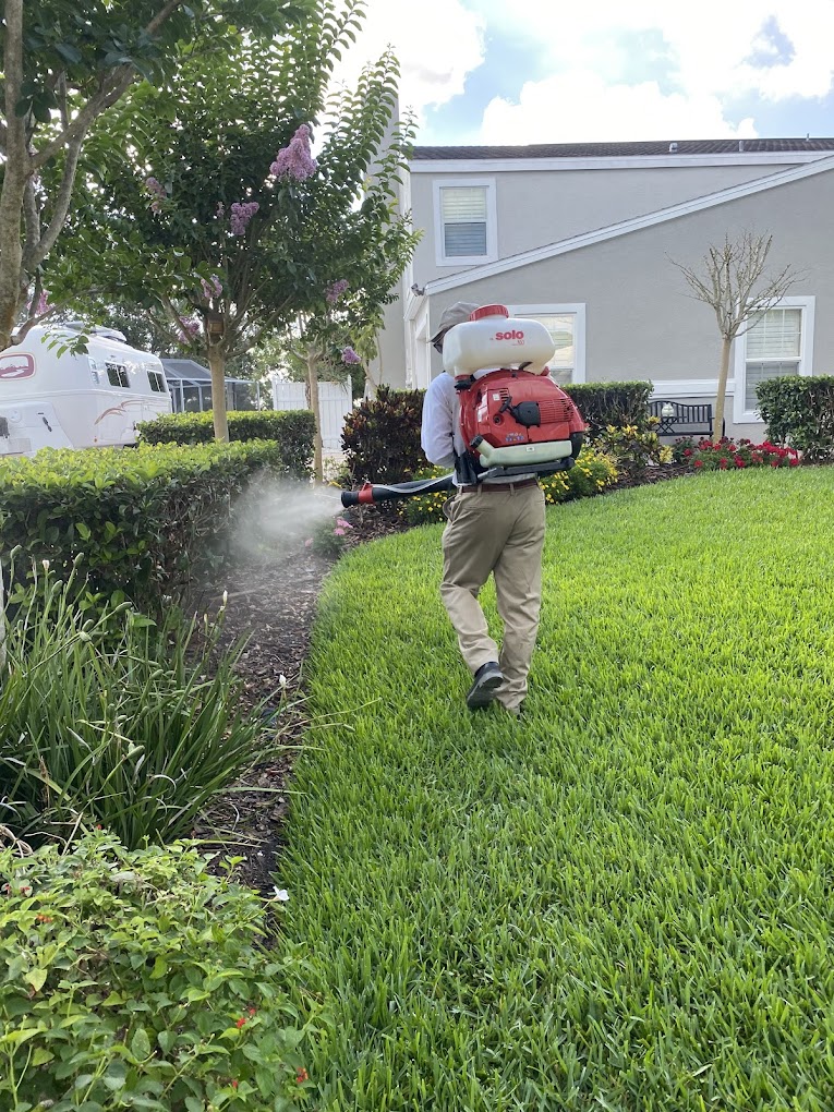 Lawn care worker spraying pesticide near residential building and trailer