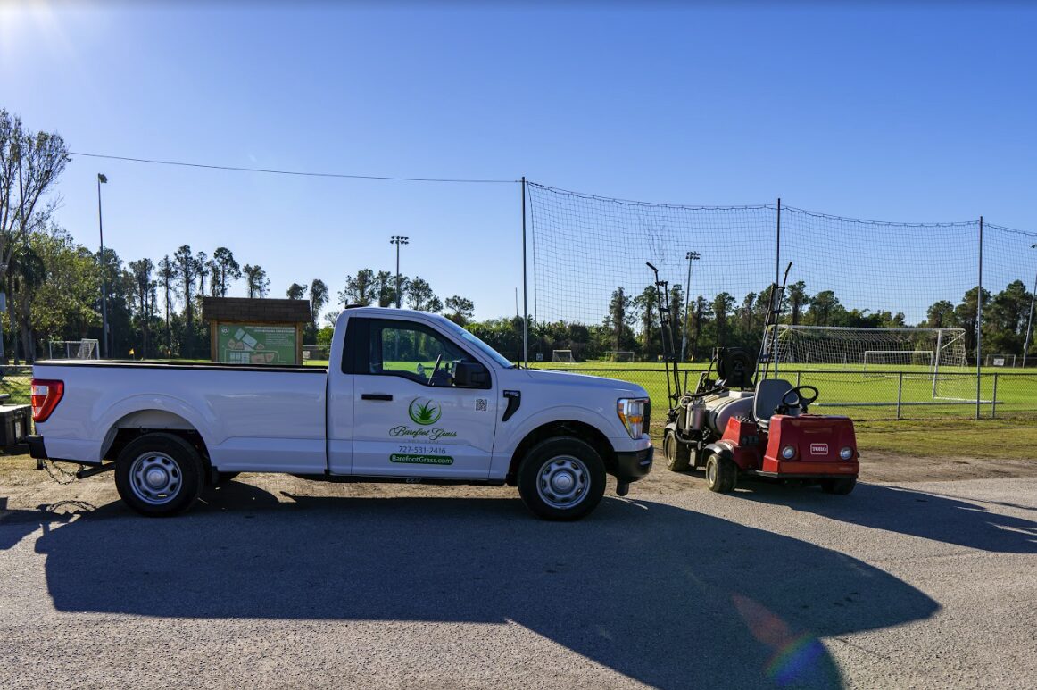 White pickup truck and red utility vehicle parked near soccer field