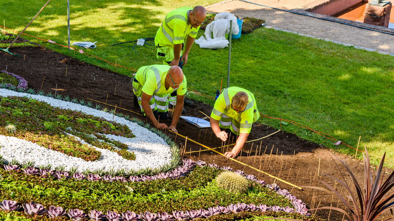 Landscapers in neon vests planting flowers and measuring garden design