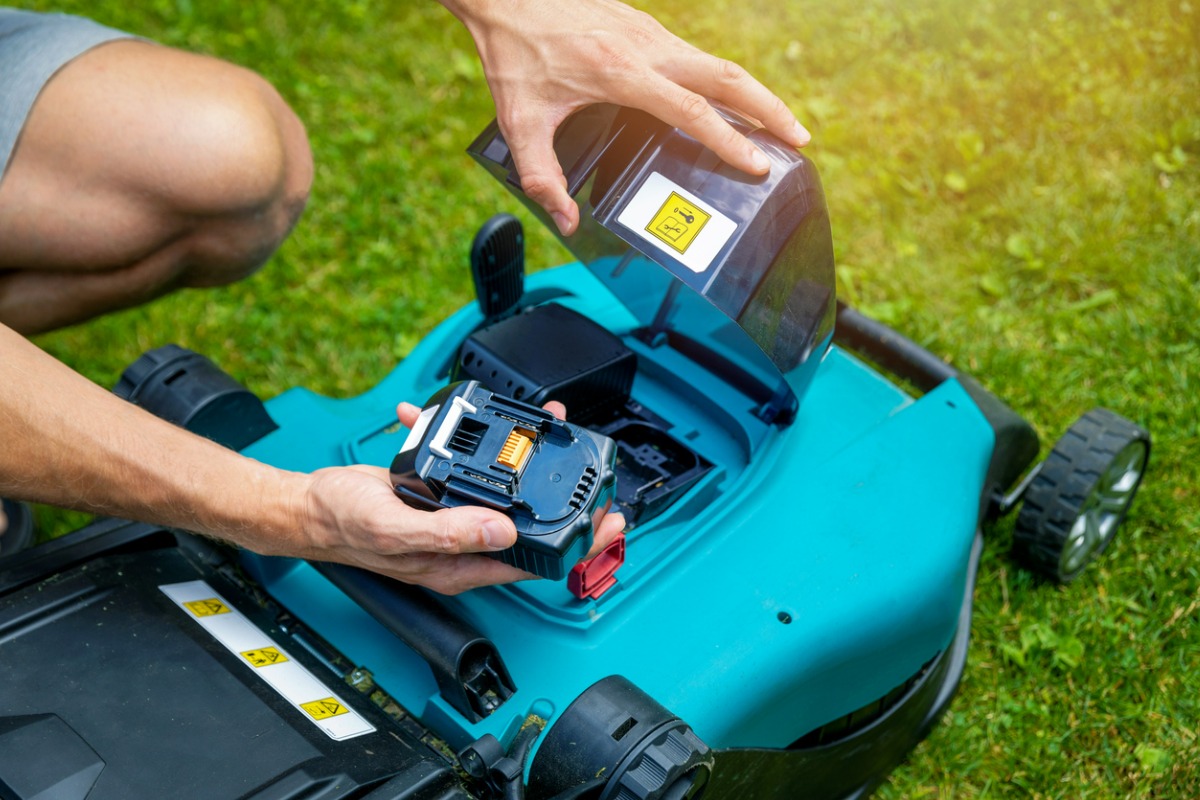 Hands inserting battery into a teal cordless electric lawn mower