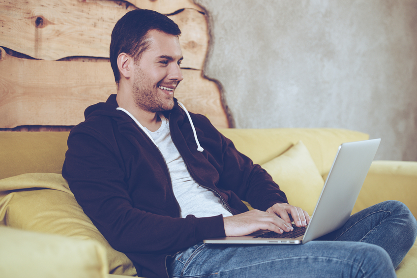 Smiling person working on laptop while sitting comfortably on yellow couch