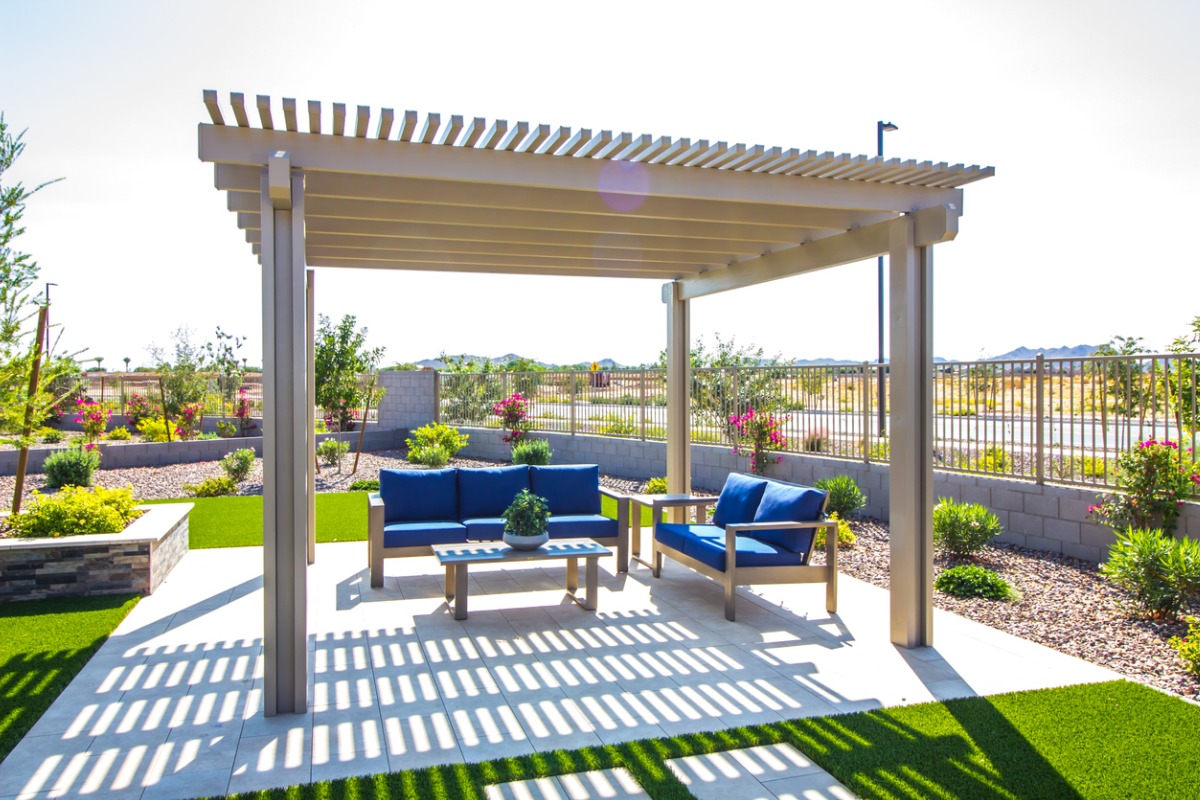 Outdoor patio with blue furniture under a white pergola, surrounded by landscaped garden