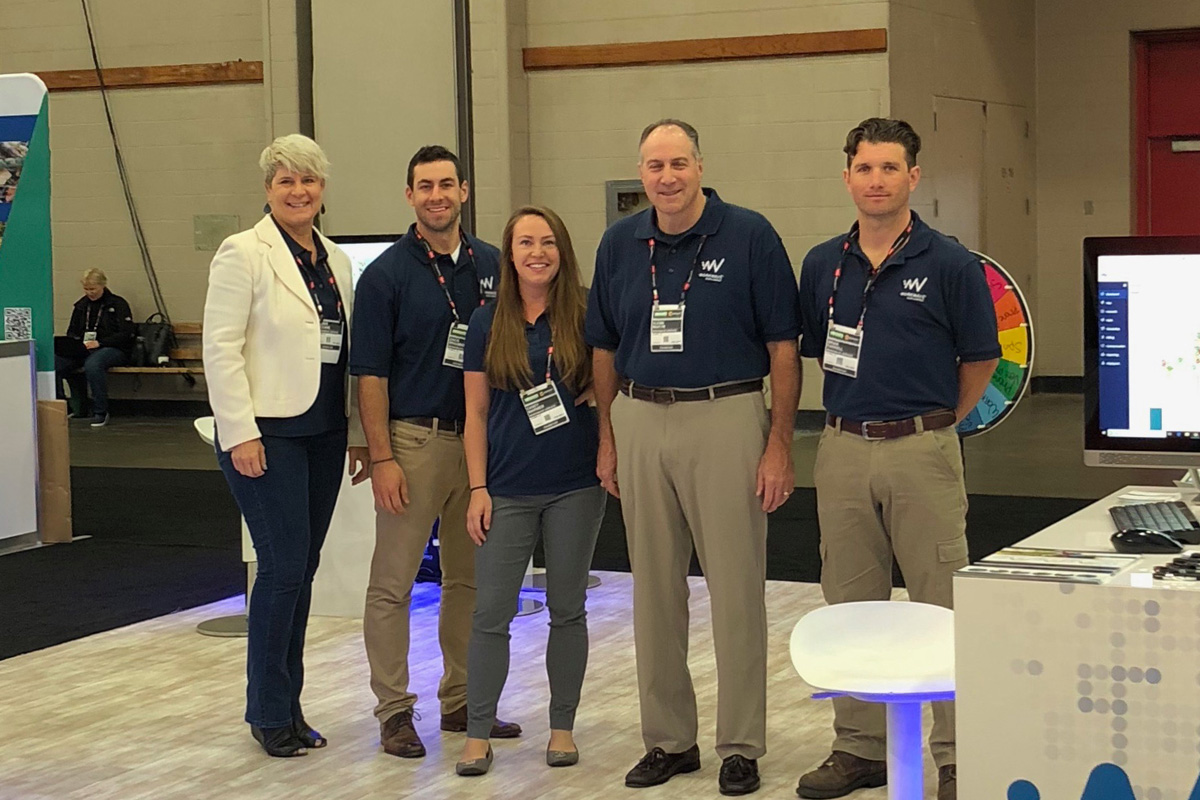 Five professionals in navy shirts stand at conference booth with technology displays