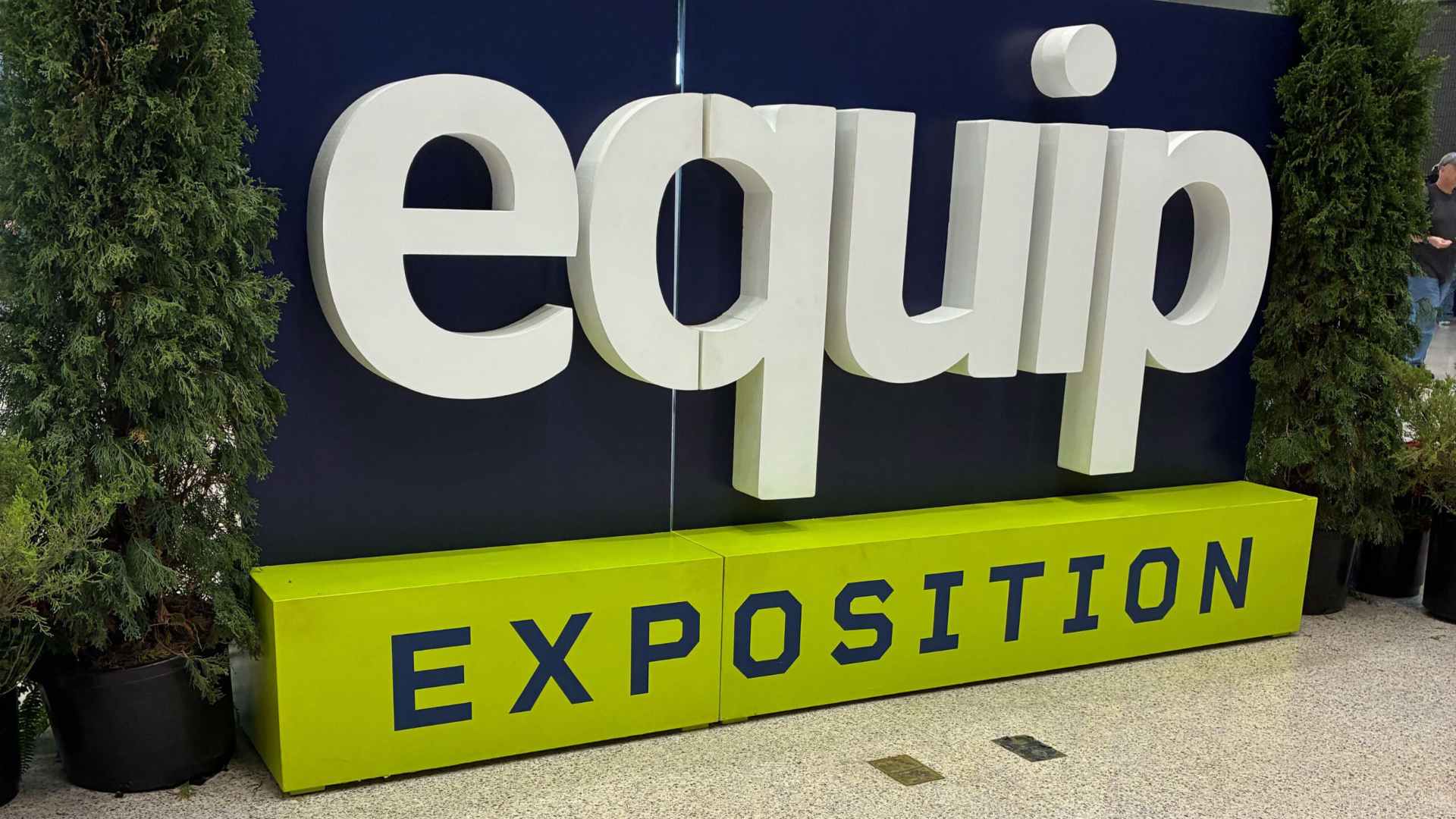 Large white "equip" logo on green "Exposition" sign with greenery