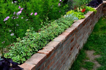 Brick garden wall lined with green plants and colorful flowers