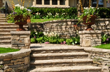 Stone steps and terraced garden with flower-filled planters near house entrance