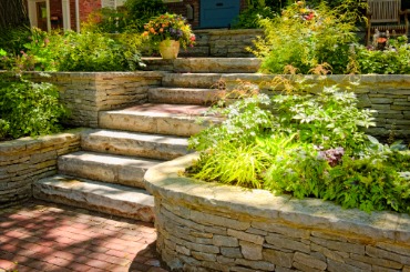 Stone garden steps with lush green plants and brick pathway