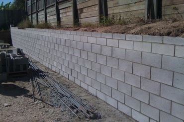 White concrete block retaining wall under construction with rebar in foreground