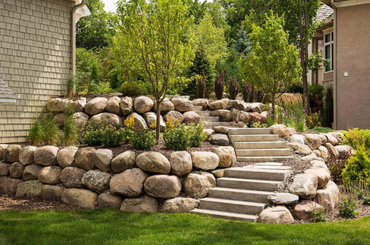 Stone terraced landscaping with steps and large boulders beside house