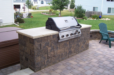 Stone outdoor kitchen with built-in grill on patio near residential backyard