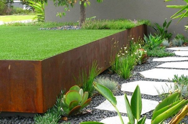 Modern garden with rusty metal planter, stone path, and green plants