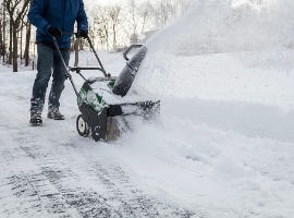 Person using snowblower to clear snowy path on winter day