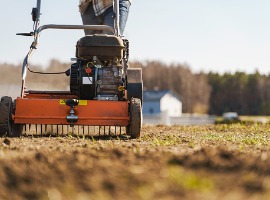 Lawn roller compacting soil on grass field with trees in background