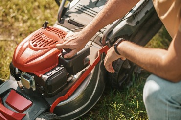 Person starting red lawn mower on grassy lawn