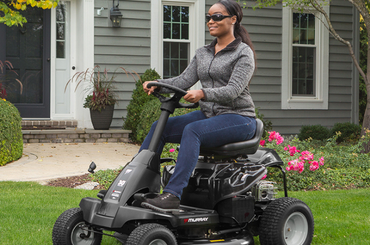 Person riding a black riding lawn mower in front of a house