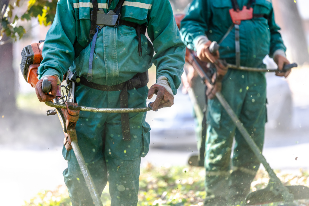 Workers in green uniforms using string trimmers to maintain outdoor landscaping