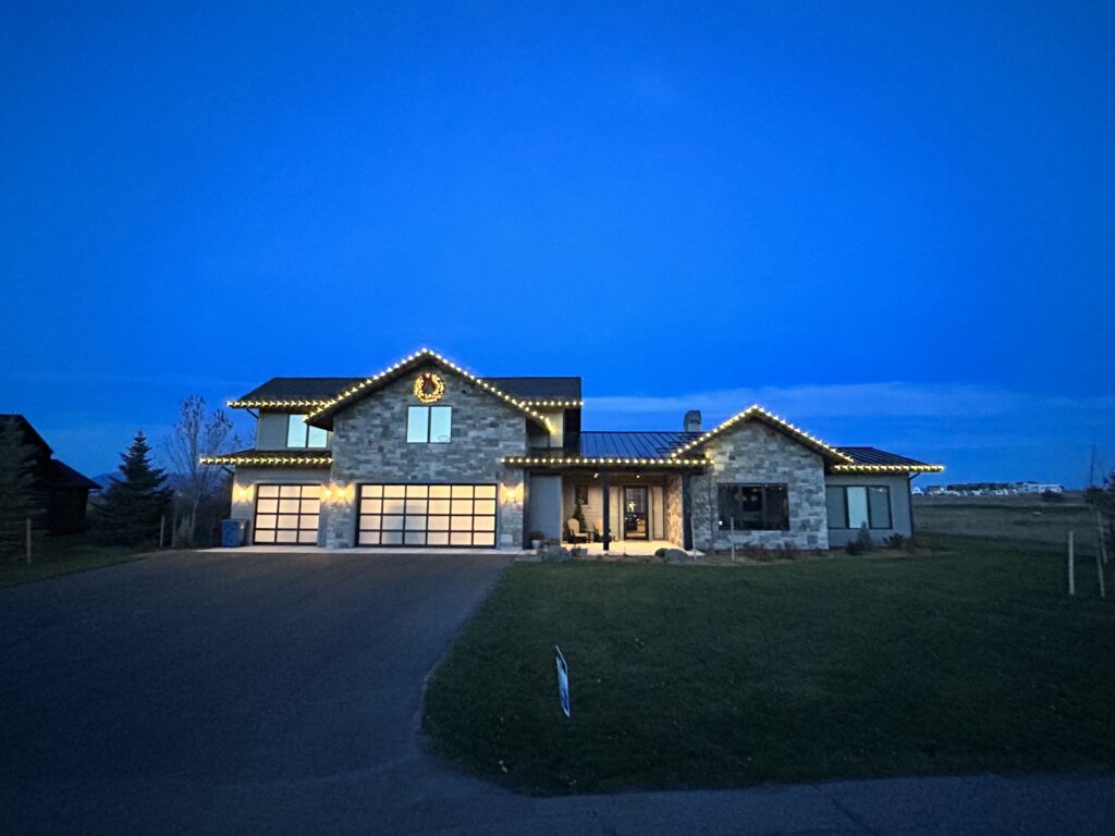 Stone house with Christmas lights at dusk, illuminated garage and blue sky