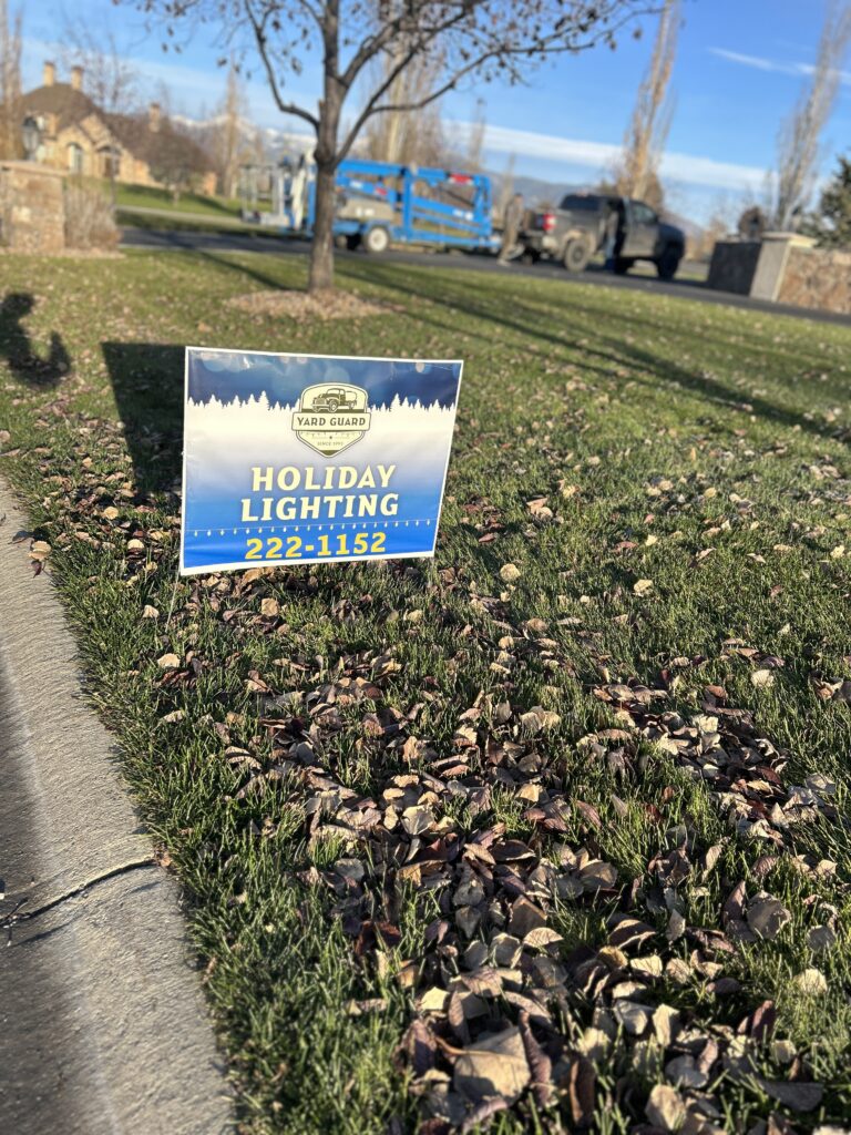 Blue yard sign for holiday lighting service on autumn lawn with leaves