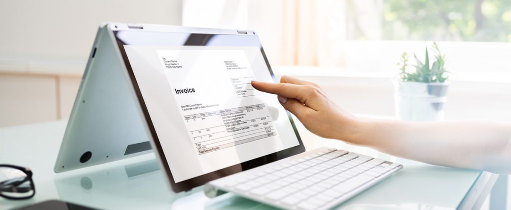 Hand pointing at digital invoice on laptop screen in bright office