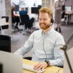 Smiling man with headset working at computer in modern office