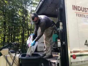Worker mixing fertilizer near industrial truck in wooded area