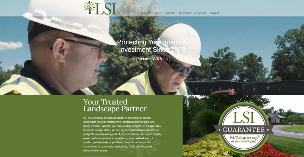 Two workers in hard hats and safety vests discussing landscape project