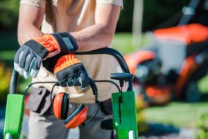 Person mowing lawn with protective gloves on garden equipment