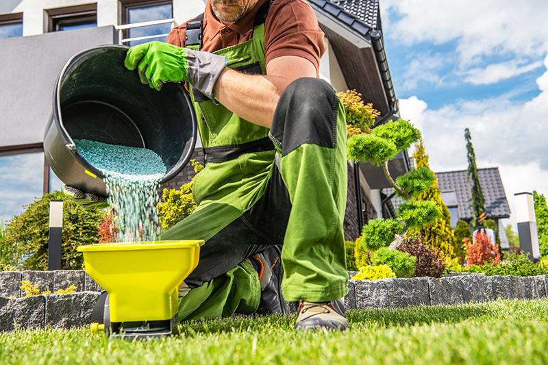 Gardener in green outfit pouring blue granules into yellow container