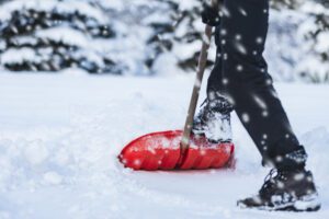 Person shoveling snow with a red snow shovel during winter storm