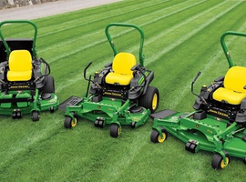 Three green and yellow zero-turn lawn mowers lined up on grass