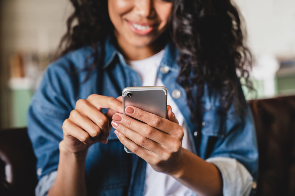 Smiling person in denim jacket using smartphone with both hands