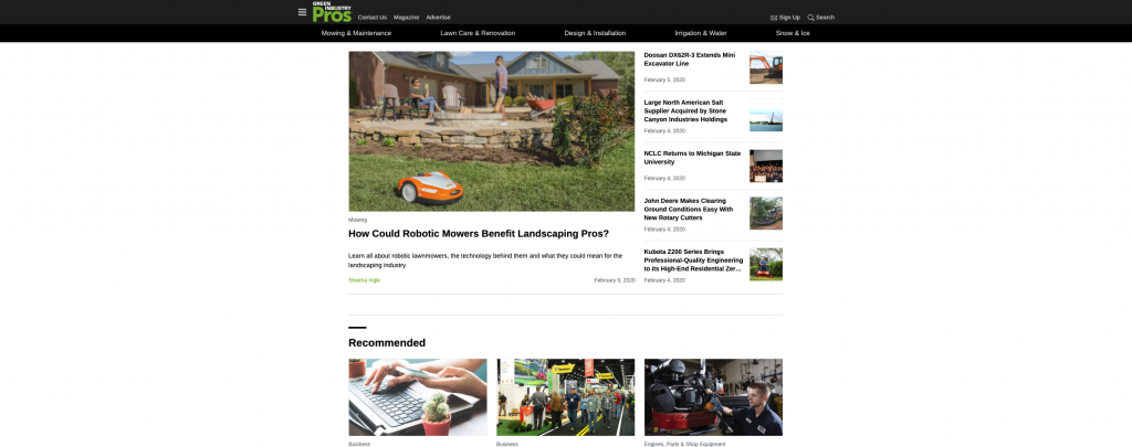 Orange robotic lawn mower in landscaped yard near stone retaining wall