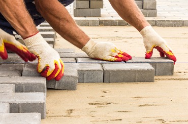 Worker laying concrete pavers on construction site with protective gloves