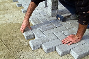 Worker laying interlocking concrete pavers on a sand base