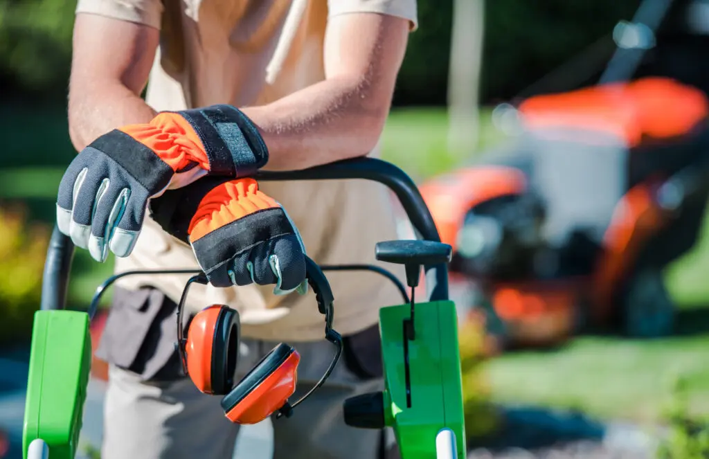 Gardener with protective gloves and earmuffs using lawn mower outdoors