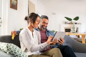 Couple sitting on couch smiling while looking at tablet together
