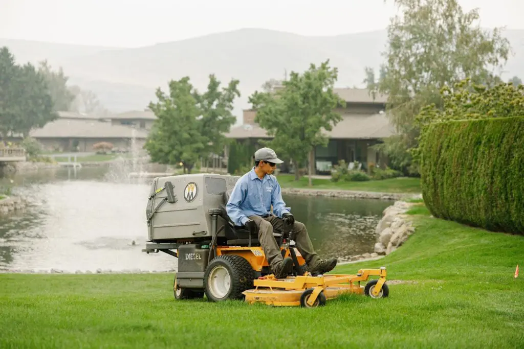 Groundskeeper mowing green lawn near pond with zero-turn yellow mower