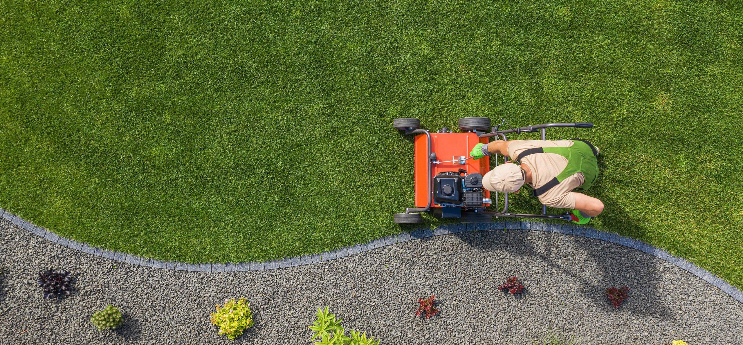 Person using lawn mower on green grass next to stone landscaping
