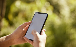 Hand holding smartphone with blank screen in blurry green outdoor setting