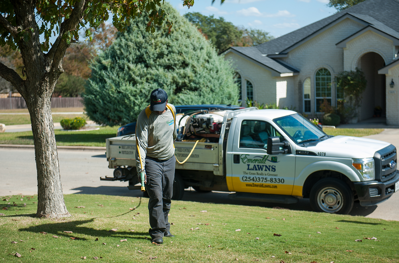 Lawn care worker spraying treatment near residential house and truck