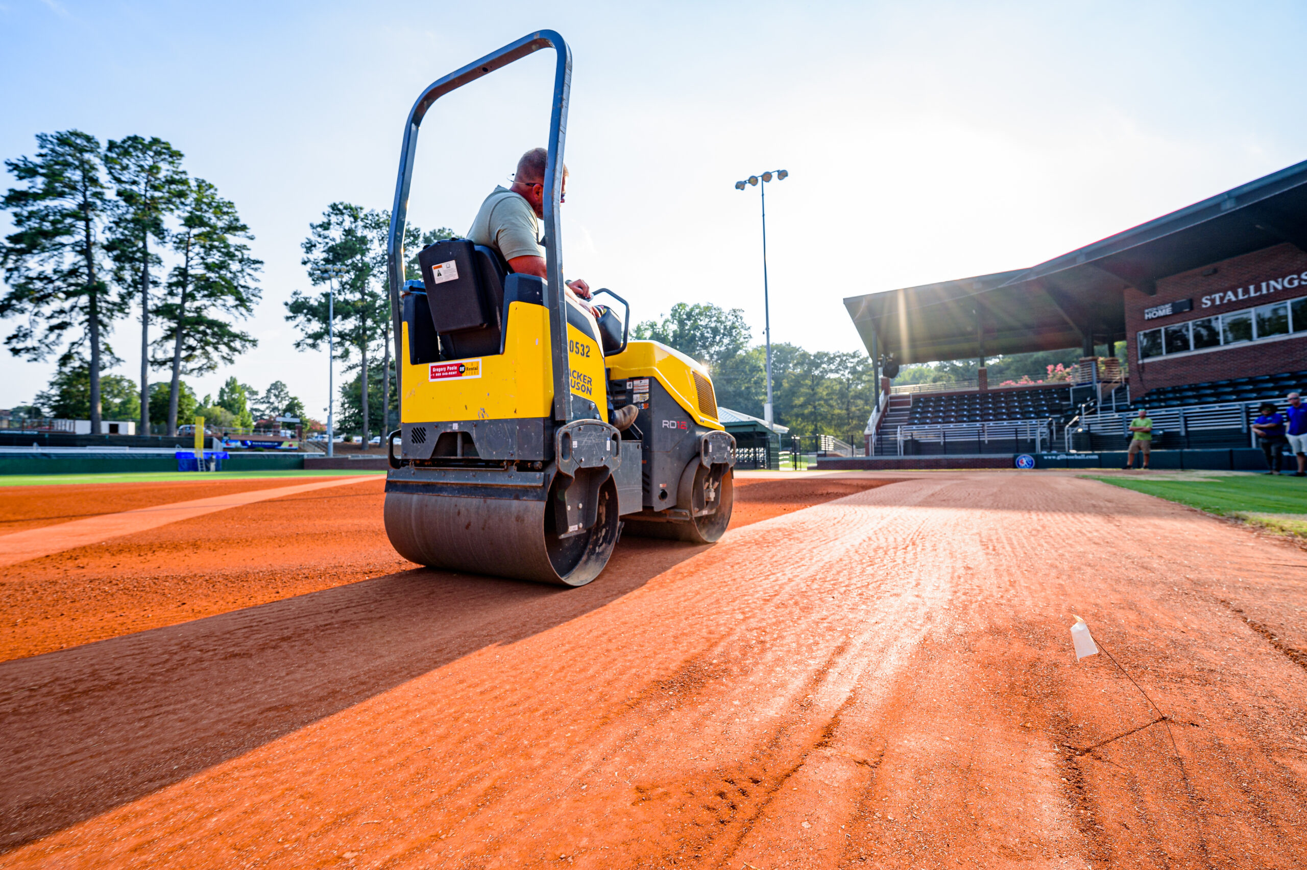Yellow roller compacting baseball field dirt on sunny day