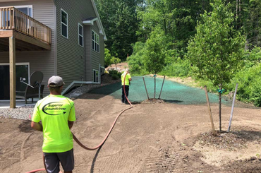 Workers spray hydroseeding on bare soil around new house construction site