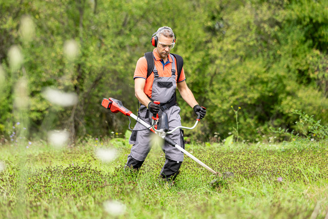 Worker in safety gear using string trimmer to maintain grassy outdoor area