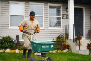 Lawn care worker spreading fertilizer on residential yard near house