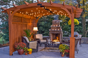 Wooden pergola with string lights, outdoor fireplace, and cozy seating area